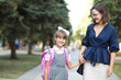 Woman and girl pupil of primary school  with backpack go hand in hand.