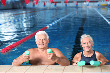 Wall Mural - Sportive senior couple with swimming noodles in indoor pool