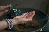 Fototapeta Lawenda - Water from drinking fountain flows into woman's hand in botanic garden.
