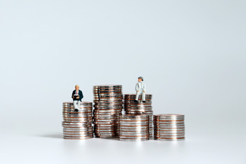 Two elderly men sitting on a pile of coins at different heights.