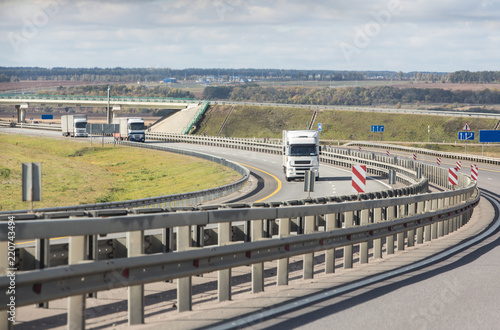 Fototapeta Karawana białych ciężarówek porusza się w linii na autostradzie kraju