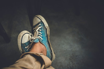 Man wearing old blue sneakers in brown trousers sitting on coffee shop,Vintage tone.Selective focus