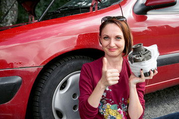 a young girl sits near a broken car and makes repairs to the electric generator, fixed it with a bandage and shows a successful gesture