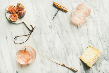 Flat-lay of glass of rose wine with ice cubes, cheese and fresh figs over marble background. Summer wine and snack set, top view, copy space