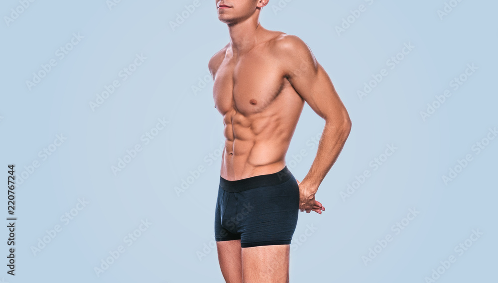Image of fitness male model in black underwear showing his abdominal torso on a blue background. Portrait of sporty healthy strong athletic man with sexy abdomen posing in studio. Healthy lifestyle - obrazy, fototapety, plakaty 