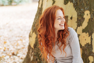 Smiling young woman leaning against a tree trunk