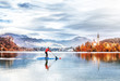 © Feel good studio - SUP sportsman workout on Picturesque lake Bled in Slovenia. Breathtaking autumn environment - forest with golden leaves, old church on the island, medieval castle on the hill top beneath dramatic sky.