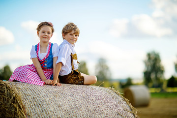 Two kids, boy and girl in traditional Bavarian costumes in wheat field with hay bales