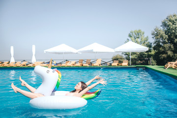 Wall Mural - Happy and satisfied girl is lying on air mattress in the middle of swimming pool. She keeps hands and legs in air. Girl is relaxing. She has some rest.