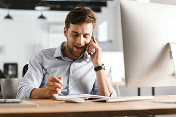 Poster - Pleased business man talking by smartphone and writing something