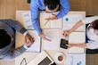 © DragonImages - From above shot of coworkers sitting at table with papers and calculating while having meeting