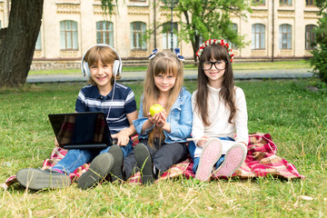 One boy and two girls, schoolchildren are sitting on the grass. Learn in junior school. Spend time together. Three friends.