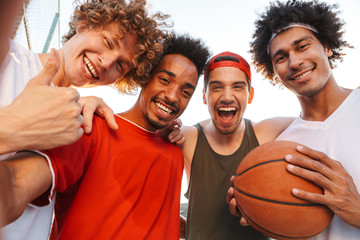 Wall Mural - Photo closeup of muscular sporty men smiling and taking selfie, while playing basketball at playground outdoor during summer sunny day