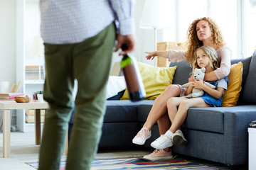 Young woman forbidding her husband to drink alcohol at home while siting on sofa with little daughter