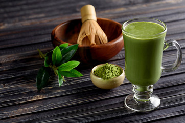 Matcha green tea latte beverage in glass cup on dark wooden background