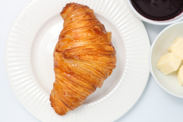 Wall Mural - Freshly baked croissant, jam and butter slices on a light background