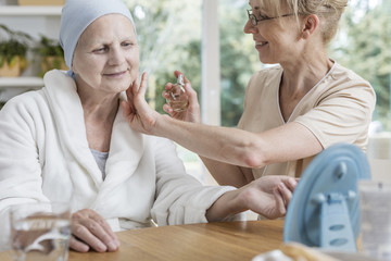 Sticker - Happy caregiver spraying perfumes on sick senior woman with breast cancer