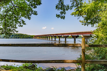 View Over Split Rail Fence Of Bridge Over The Tennessee River On The Natchez Trace Parkway In Mississippi, USA, With Blue Sky And Framed On Both Sides By The Spring Green Of Hardwood Branches.
