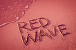 'RED WAVE' written in the sand on the beach with the sea washing up the shore.