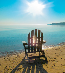 Landscape with coast, water, sun with bright sunbeams in the sky and beach chair. Beautiful morning view of Lake Huron, the Great Lakes region, USA.