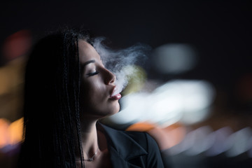 Woman smoking at night, city lights background