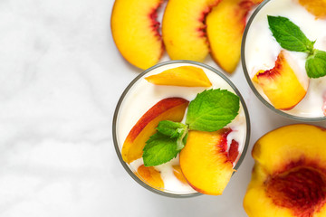 Wall Mural - two glasses of healthy fruit yogurt with fresh peaches and mint on white marble table. healthy breakfast. top view