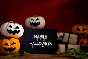 Wall Mural - White and yellow ghost pumpkin on wooden table with bat on orange background. halloween concept.