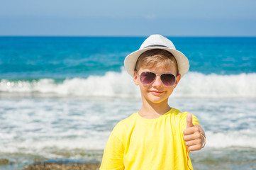 Wall Mural - boy in a summer hat by the sea showing thumbs up