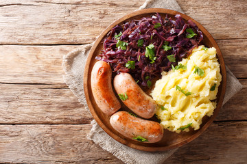 Roasted sausages with steamed cabbage (sauerkraut) and boiled potatoes close-up on a plate. Horizontal top view