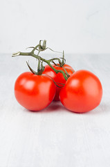 Wall Mural - Colorful red ripe tomatoes on green branch on white wood board, copy space, vertical, closeup.