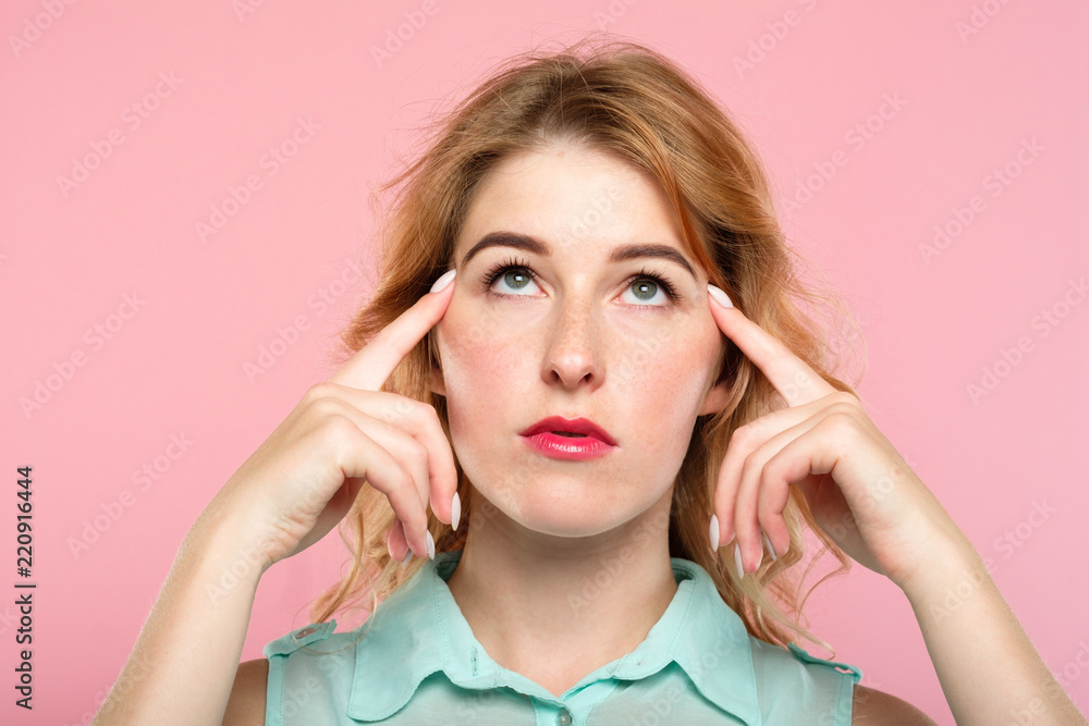 mind games telepathy thought transfer and brain power. beautiful girl concentrating on invisible object above her. index fingers on temples. young beautiful blond woman portrait on pink background. - obrazy, fototapety, plakaty 