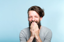 Joyful Excited Happy Smiling Man Covering Mouth With Hands. Portrait Of A Young Bearded Guy On Blue Background. Emotion Facial Expression. Feelings And People Reaction.