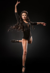 Wall Mural - smiling ballerina in black bodysuit and ballet shoes dancing on dark backdrop