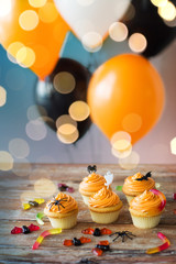 Wall Mural - food, baking and holidays concept - cupcakes or muffins with halloween party decorations and jelly candies on wooden table and balloons over lights