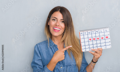 Cuadros en Lienzo Young adult woman over grey grunge wall showing period calendar very happy point