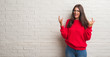 © Krakenimages.com - Young brunette woman standing over white brick wall shouting with crazy expression doing rock symbol with hands up. Music star. Heavy concept.