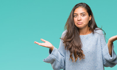 Canvas Print - Young beautiful arab woman wearing winter sweater over isolated background clueless and confused expression with arms and hands raised. Doubt concept.