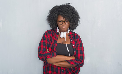 Canvas Print - Young african american woman over grey grunge wall wearing headphones skeptic and nervous, disapproving expression on face with crossed arms. Negative person.