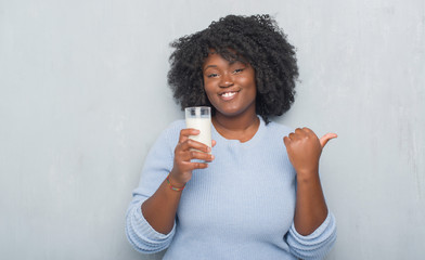 Sticker - Young african american woman over grey grunge wall drinking a glass of milk pointing and showing with thumb up to the side with happy face smiling