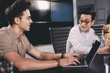 Wall Mural - young asian businessman talking to colleague while he using laptop at modern office