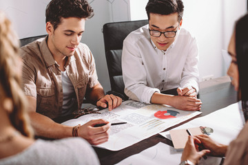 Wall Mural - two multiethnic businessmen having meeting at table with graphs in modern office