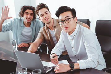 Wall Mural - three multicultural businessmen at table with laptops in modern office