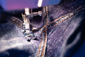 Wall Mural - Repair jeans on the sewing machine. View of the fabric, needle and thread. Illumination from the built-in incandescent lamp. Jeans are a type of trousers, typically made from denim or dungaree cloth.