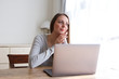 © mimagephotos - young woman sitting at home with laptop and looking out of window