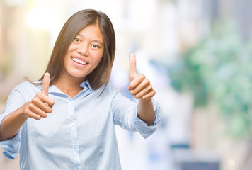 Young asian business woman over isolated background approving doing positive gesture with hand, thumbs up smiling and happy for success. Looking at the camera, winner gesture.