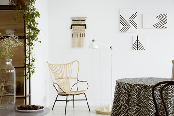 flowers on table near modern armchair in bright apartment interior with lamp and posters. real photo