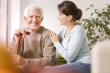 Smiling grandfather with walking stick and happy woman during meeting