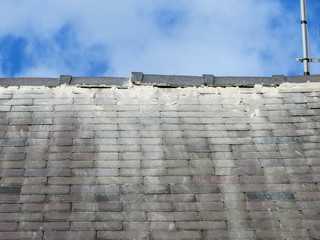 Shoddy roofing work by cowboy builder. Results of rouge worker posing as skilled tradesman. Badly pointed ridge tiles on slate roof, mortar running down tiles. Close up.