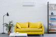 interior of modern living room with yellow couch and air conditioner hanging on white wall