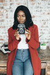 © sofiko14 - Young afro american girl in red coat in urban background holds the retro camera in her hands